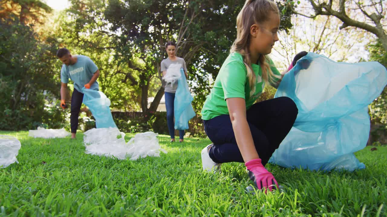 Figlia caucasica sorridente che tiene un sacco per i rifiuti, raccogliendo rifiuti di plastica con i genitori.