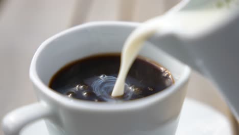 close-up of fresh milk pouring into hot black coffee in a white ceramic cup