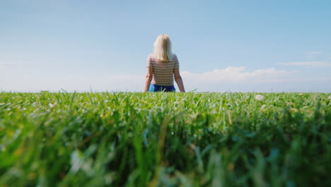 young woman in the center of a green meadow resting in nature rear view