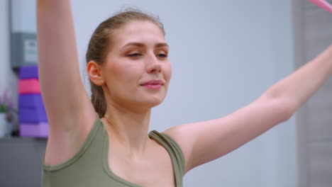 woman in green stretching with resistance band, moving from left to right in a gym with fitness equipment in the background, focused facial expression and controlled movement during exercise