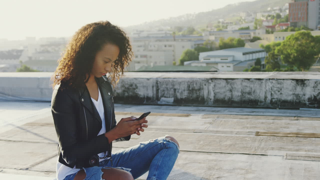 Fashionable young woman on urban rooftop using smartphone