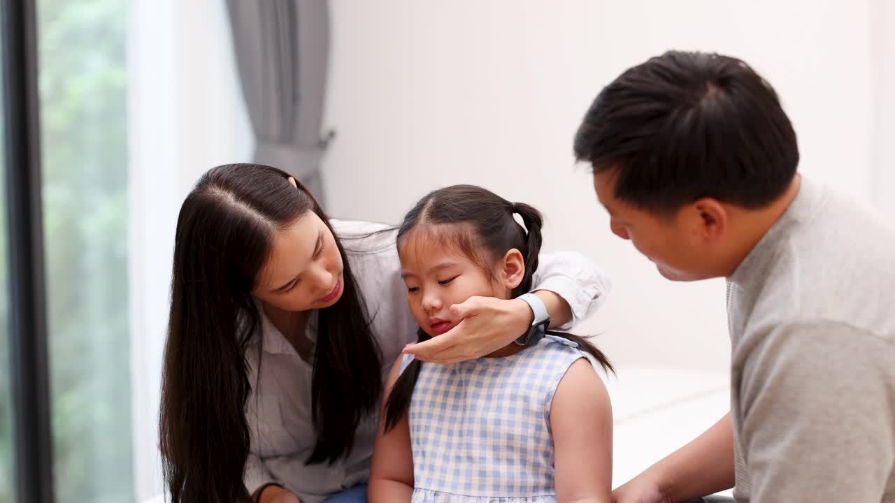 Mother and father care for ill daughter at home, checking forehead with gentle, concerned expressions