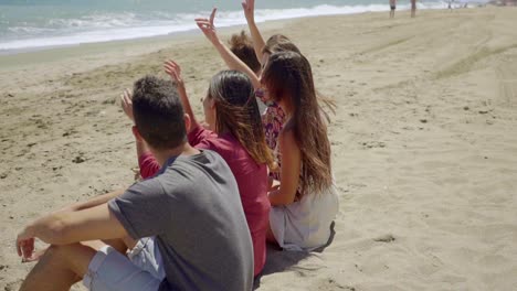 las espaldas de los adolescentes sentados en la playa de arena al aire libre