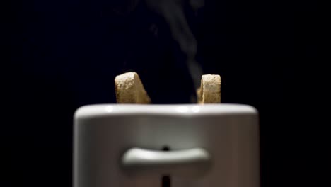 Close-up-shot-of-toast-steaming-and-popping-up-out-the-toaster-with-black-background