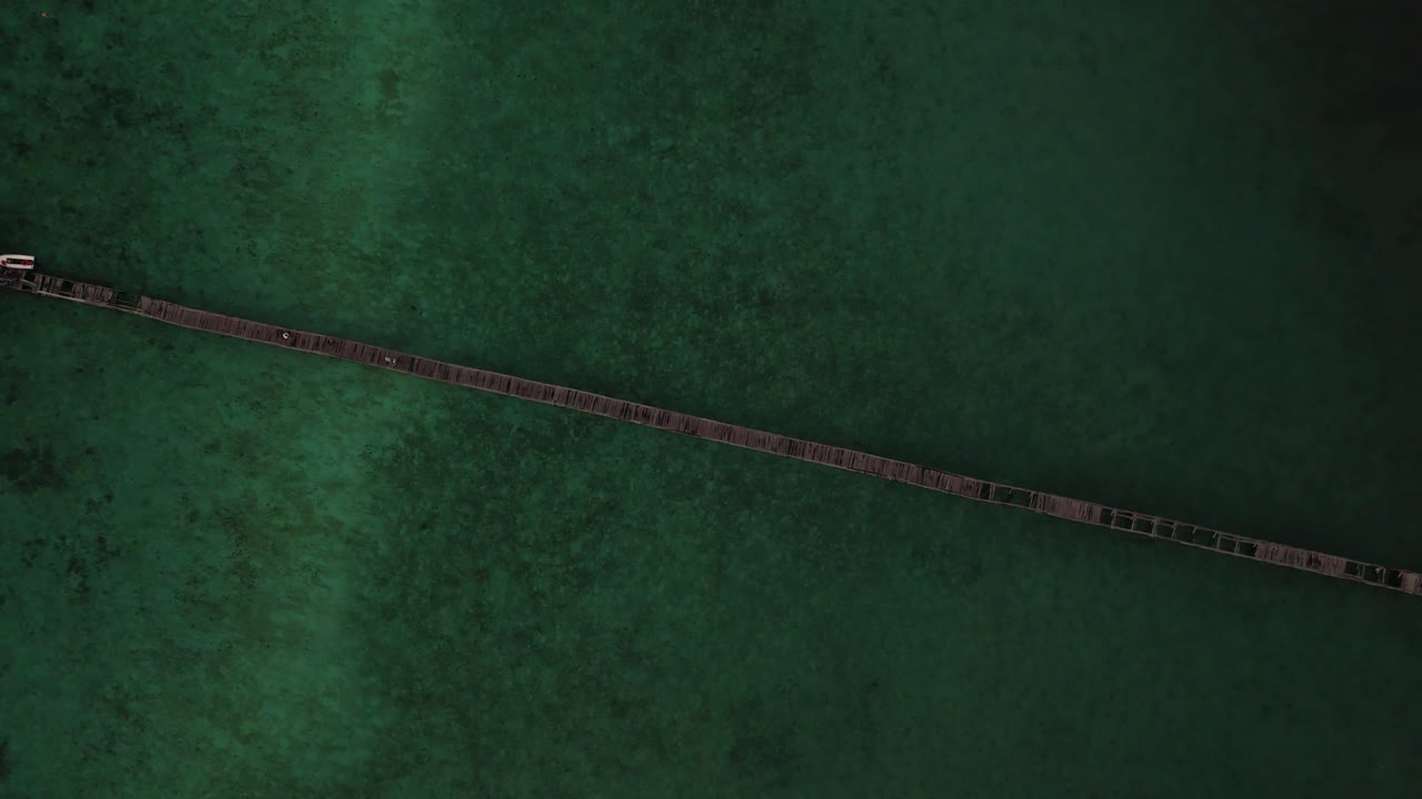 Filmato aereo dall'alto di un drone sopra la spiaggia di Manjarite nel parco nazionale di Komodo, in Indonesia, che mostra un lungo molo di legno che si estende attraverso l'acqua verde calma, acquisito in alta risoluzione 4K