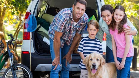 happy caucasian parents, son and daughter standing beside open car boot with pet dog in park