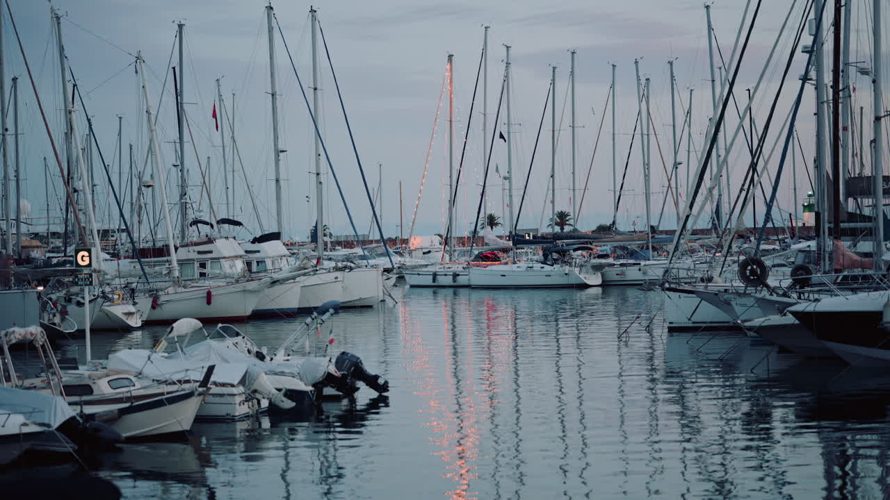 Wide shot of a marina filled with yachts and sailboats at dusk, with soft reflections on the calm water