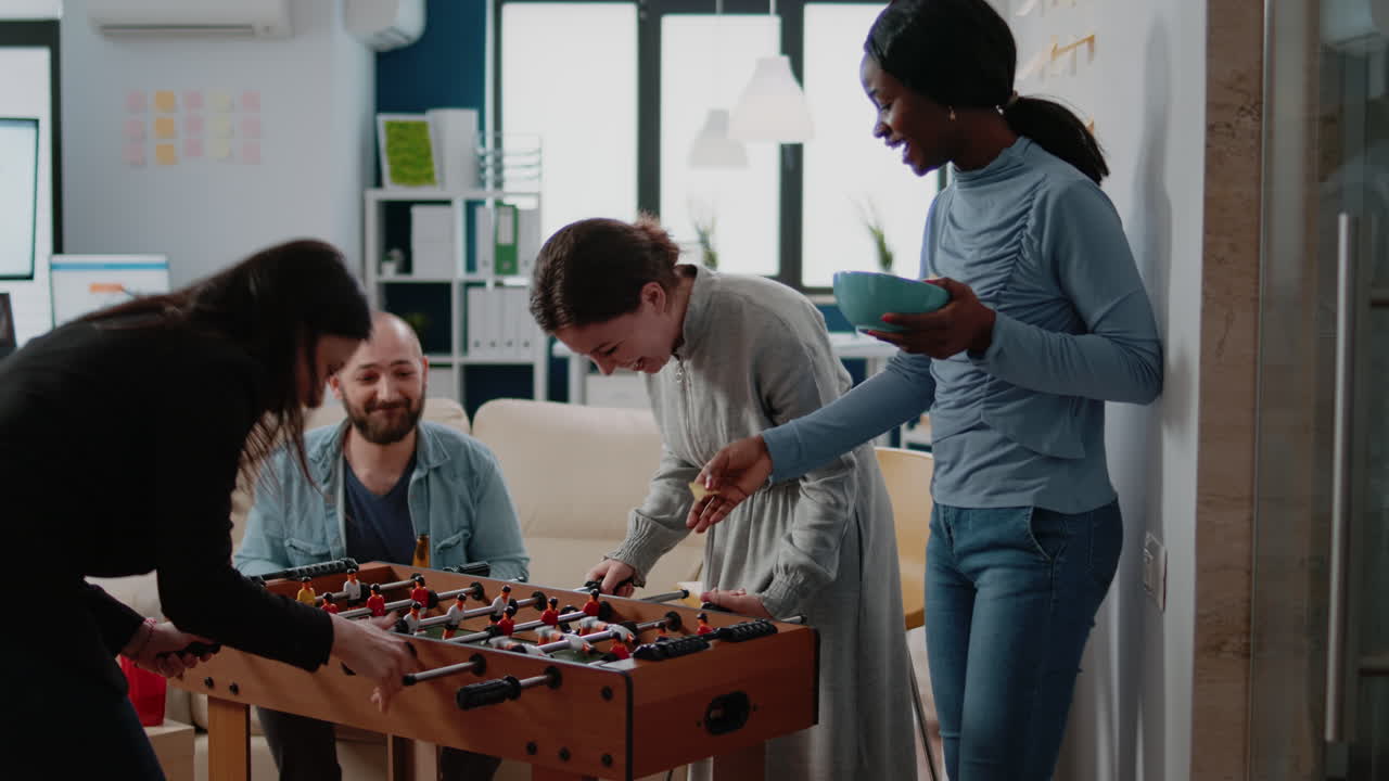 Multi ethnic coworkers playing game with foosball table