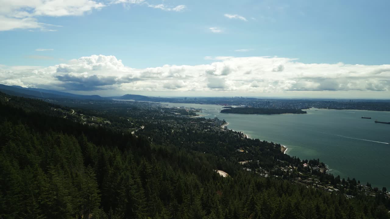 un dron volando sobre la costa soleada y la zona boscosa de las colinas de las montañas del oeste de vancouver con stanley park y el centro de vancouver en el fondo en un soleado día de verano con barcos navegando a través de la bahía.