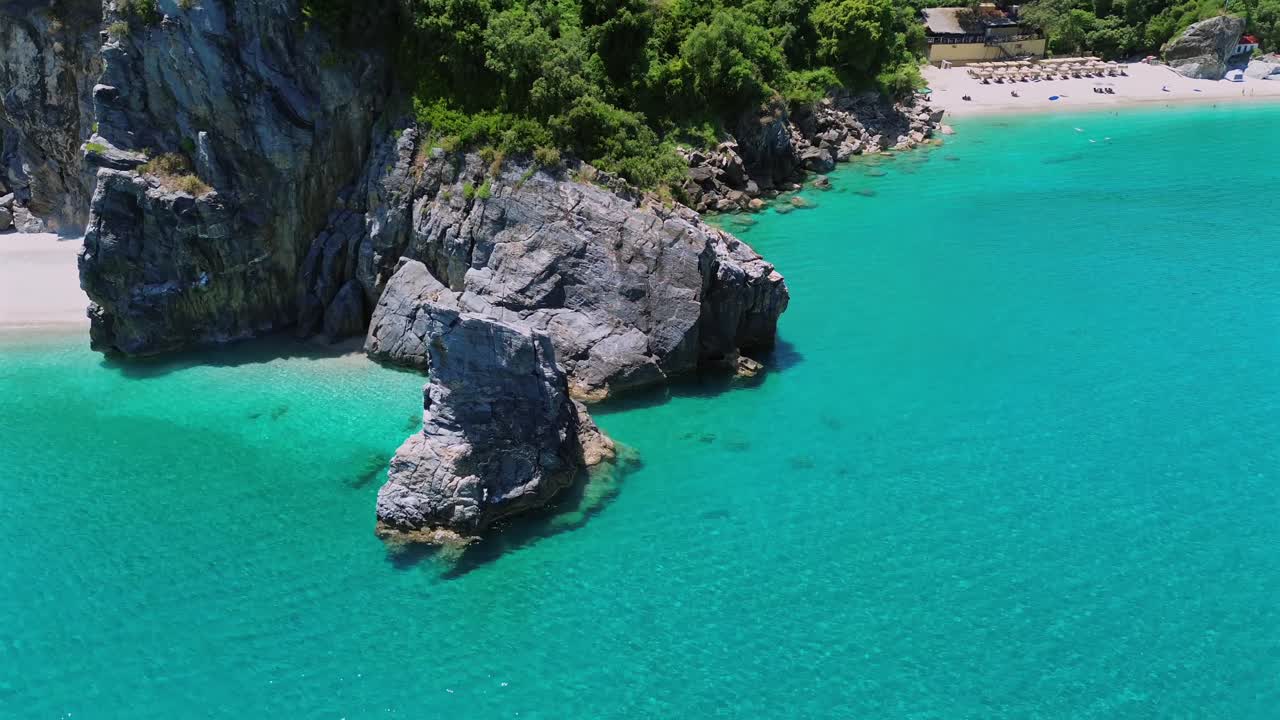 Ripresa cinematografica con drone in tracking lungo le lussureggianti scogliere verdi del Pelio. Veduta dall'alto del vivace mare Egeo turchese, della sabbia dorata e delle iconiche formazioni rocciose. Ideale per film di viaggio e sulla natura.
