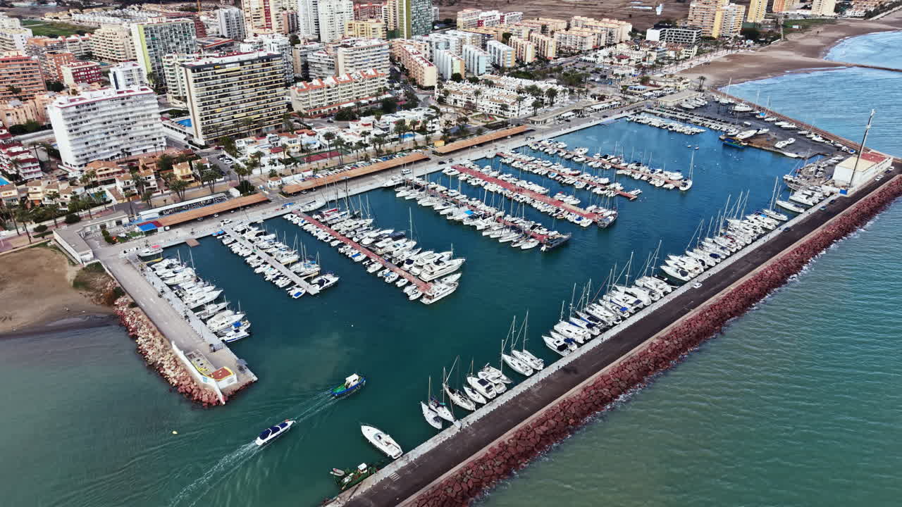 Marina con barche ormeggiate in acque cristalline vicino a edifici costieri durante il giorno in una zona vivace.