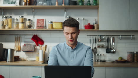 man searching information online sitting at home kitchen. guy chatting internet.