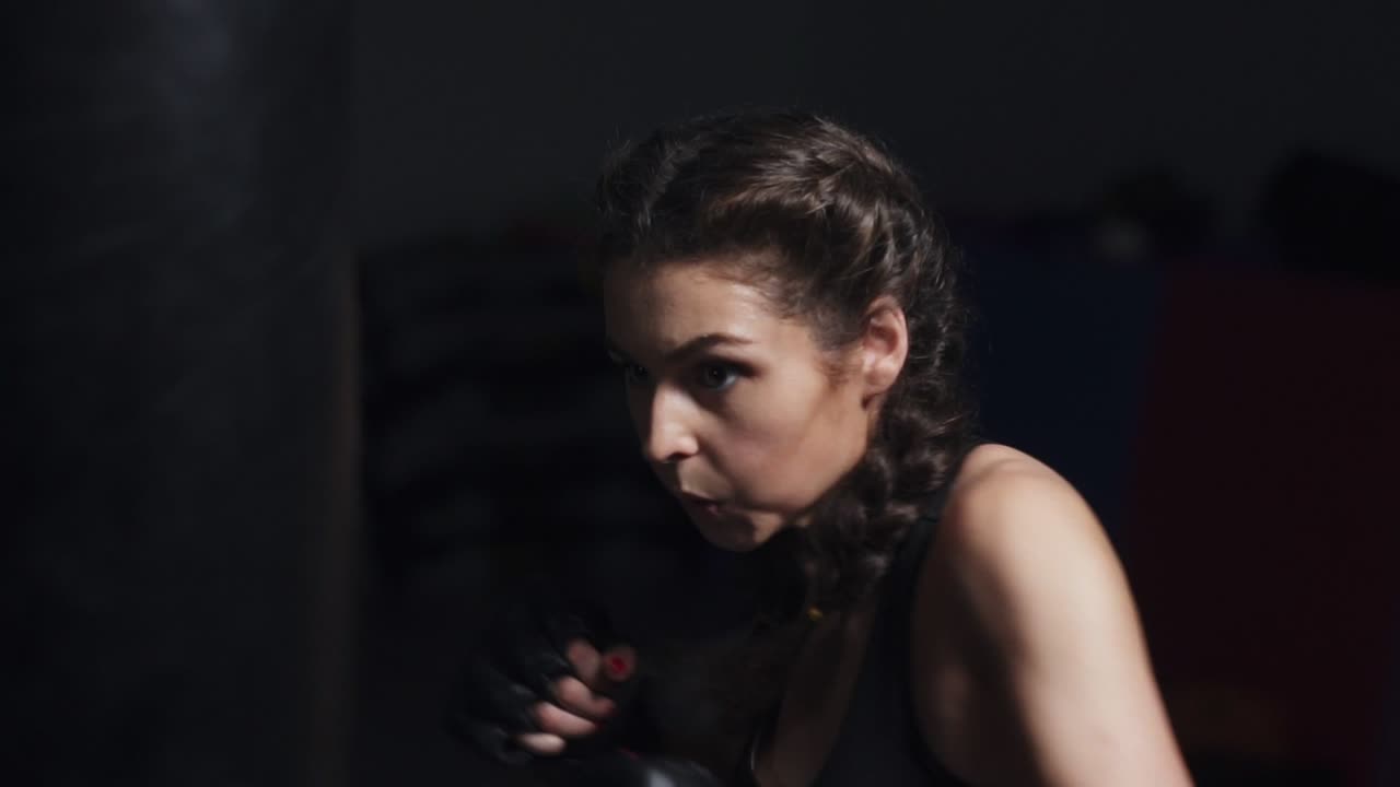 Young woman in boxing gloves training with a punching bag in a boxing club