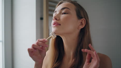 joven masajeando la cara en el retrato del baño. chica fresca usando un rodillo de jade