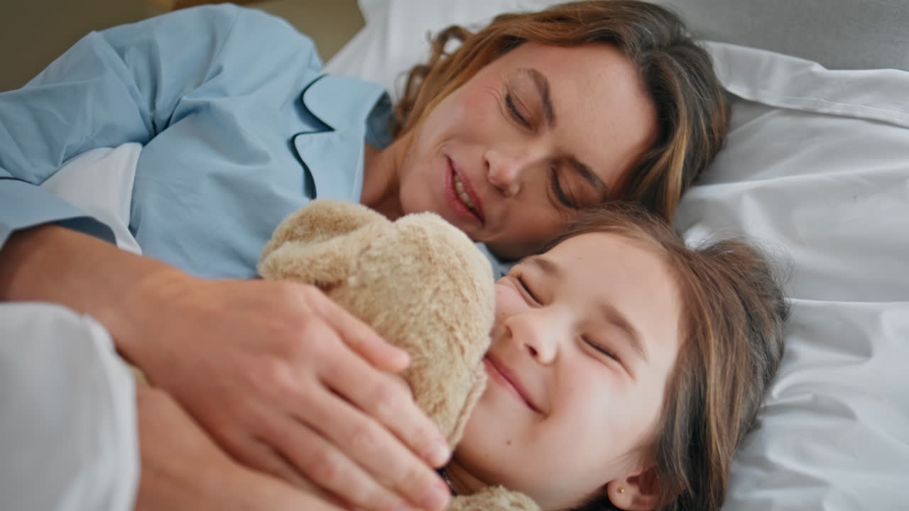 Primo piano di una famiglia spensierata che gioca con un orsacchiotto in camera da letto. Donna e figlia sdraiate sul letto