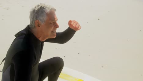 vista lateral de un surfista masculino caucásico sénior activo con ojos protectoras mirando al mar en la playa 4k