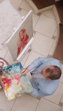 artist adds water to paint at live model drawing. professional painter makes gentle pink shade to draw woman portrait in gallery. man creates picture