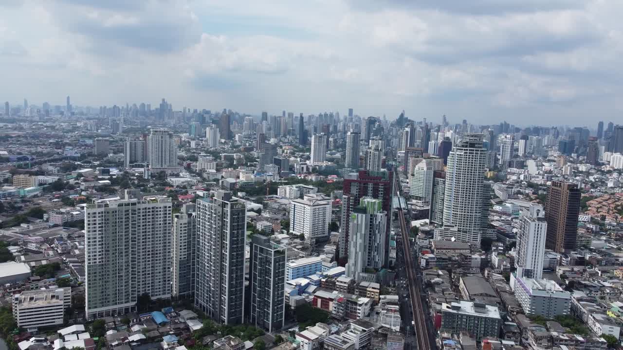 Stunning aerial footage captures Bangkok's sprawling skyline, showcasing modern skyscrapers and dense urban layout under a dynamic cloudy sky. Vibrant city life from above.