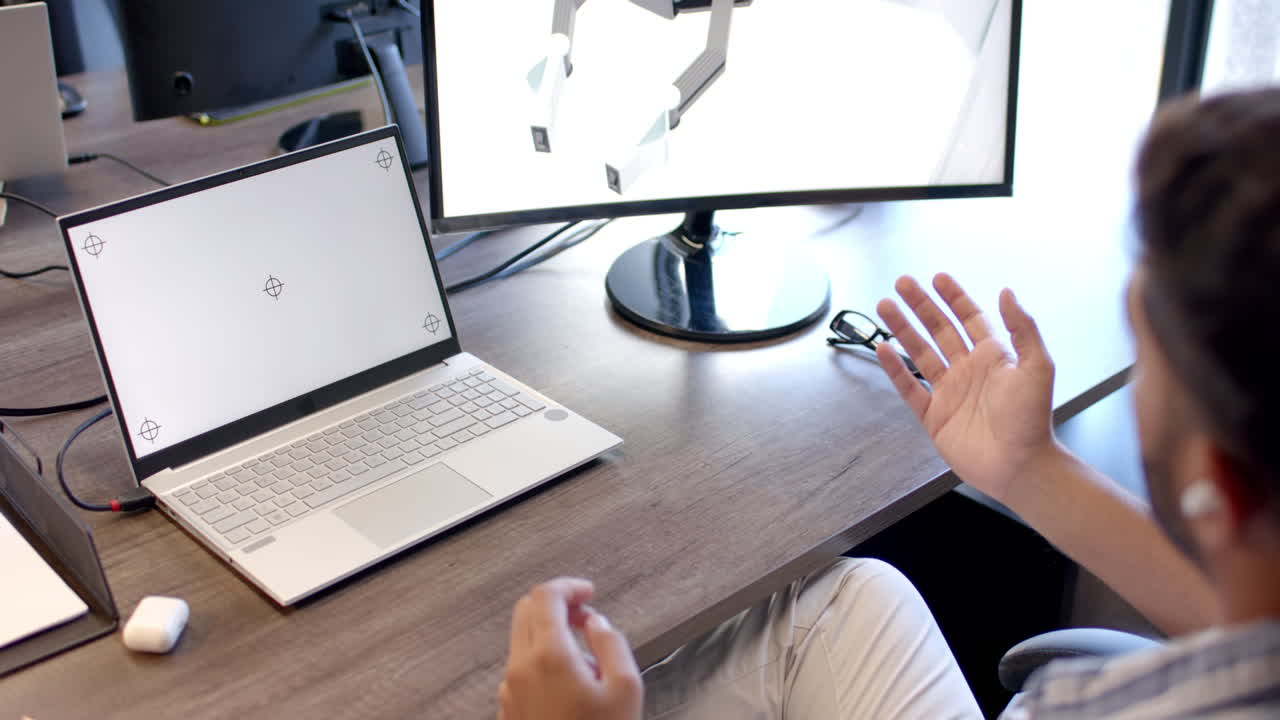 Gesturing while discussing robotic design, person using laptop and monitor in office, copy space