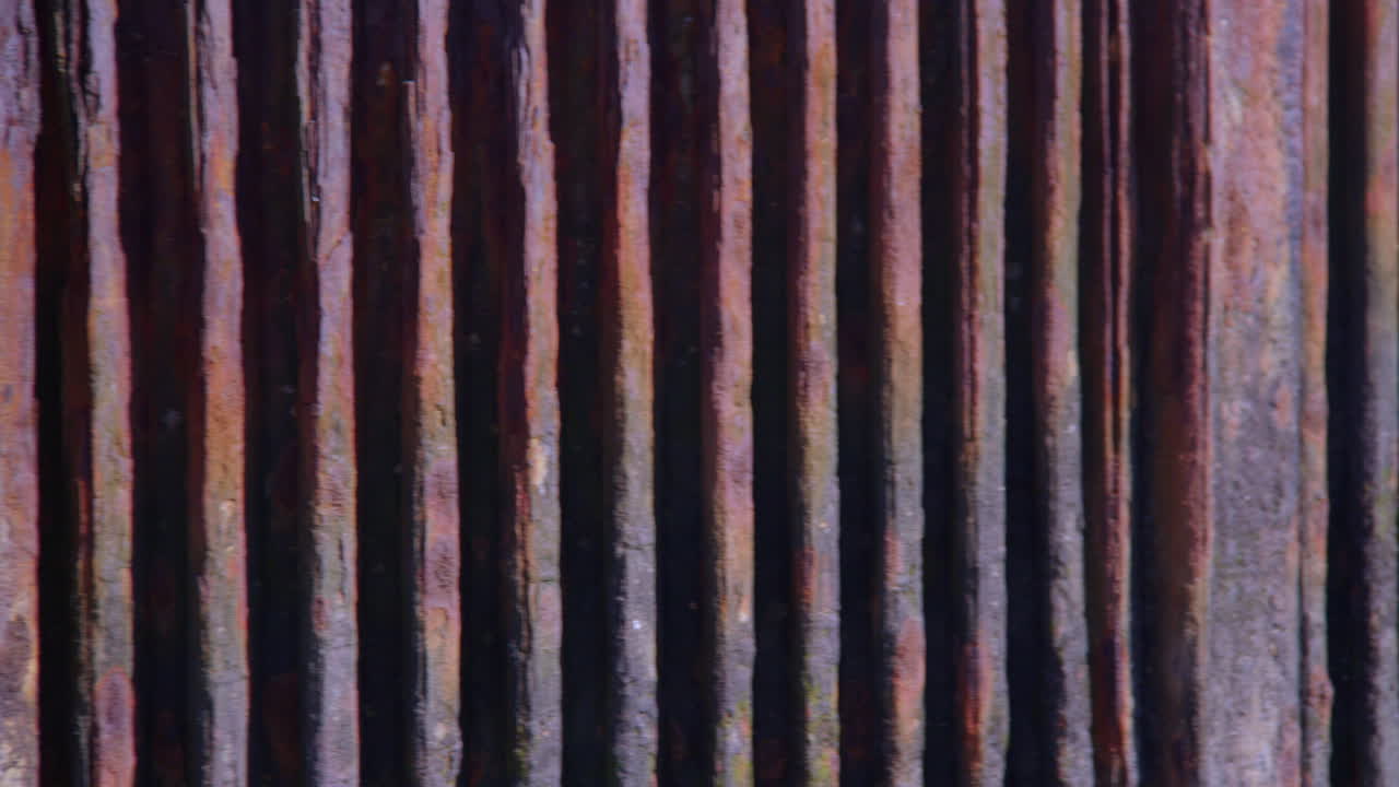 Schwenkaufnahme des rostenden Metallzauns am Wasserauslauf für das KWK-Kraftwerk Grain am Fluss Medway auf der Isle of Grain, neben dem grünen Batterieturm.