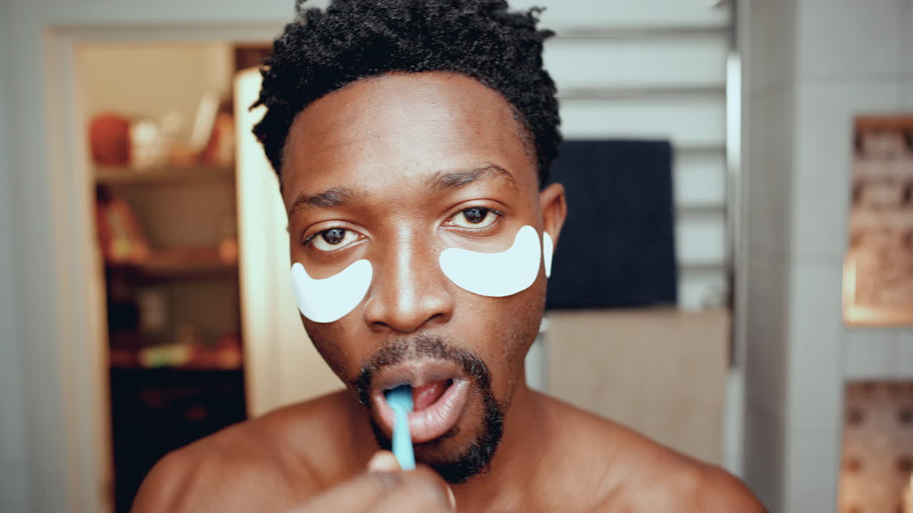 hombre afroamericano con parches debajo de los ojos cepillándose los dientes en el baño