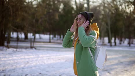 Happy-woman-dance-in-winter-park,-listening-to-music-on-the-phone-using-headphones,-spinning-around