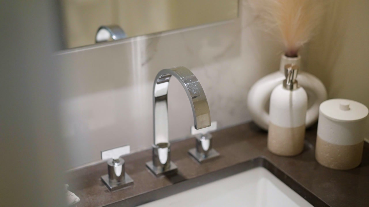 Close-up of a modern bathroom sink featuring a chrome faucet, marble backsplash, and minimalist decor in a stylish, upscale interior