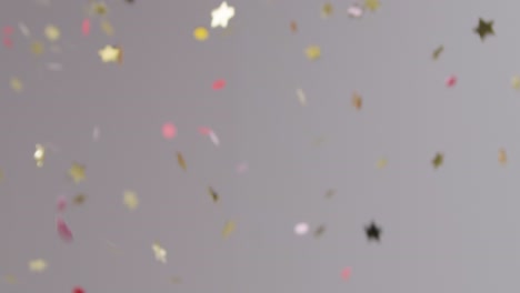 Stationary-Shot-of-Gold-and-Pink-Confetti-Falling-Against-Grey-Background