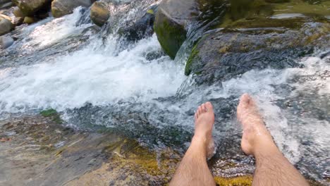 Pies-De-Un-Hombre-En-La-Corriente-De-Agua-Limpia-De-Una-Cascada