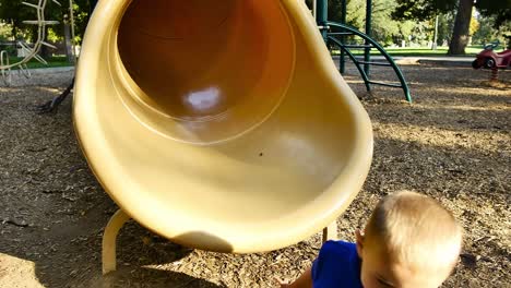 little blonde boy in blue shirt falls out of yellow tube slide