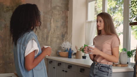 Black-girl-and-caucasian-young-woman-talk-and-laugh.-Two-female-friends-have-a-cup-of-coffee-in-the-kitchen.-Medium-shot.