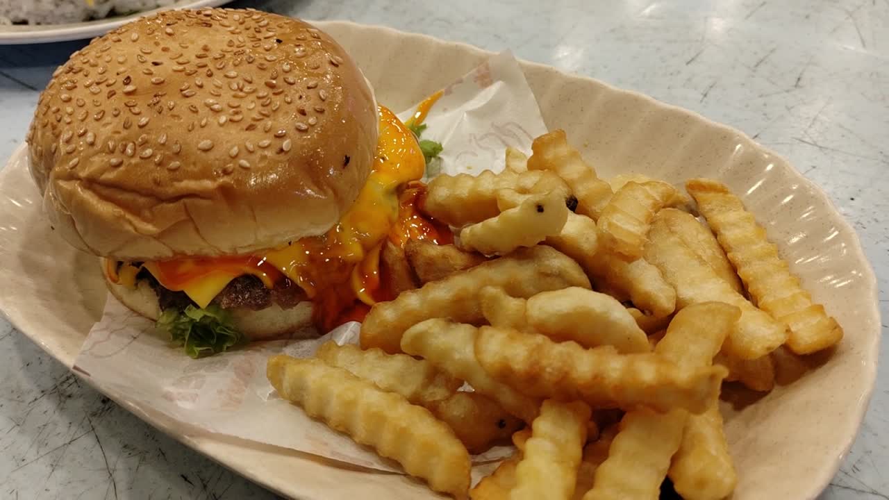 una hamburguesa con queso con carne de res y queso, elegantemente servida con papas fritas crujientes en un plato ovalado.