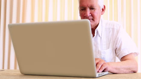 hombre mayor sentado en la mesa usando una computadora portátil