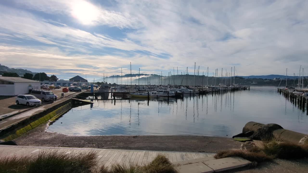 Scenic marina with boats reflecting in calm water under a cloudy sky