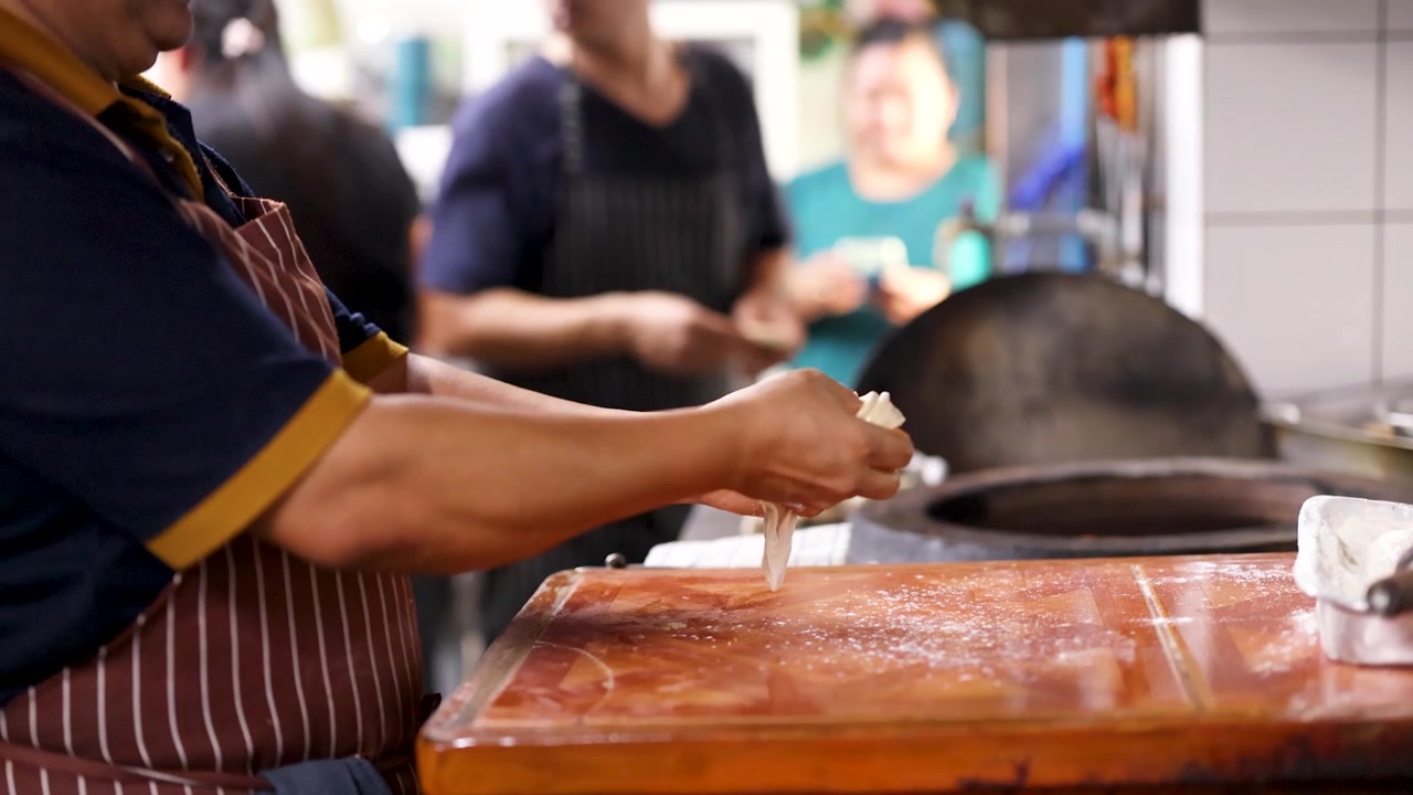 Primo piano di uno chef che impasta l'impasto su una superficie di legno infarinata in una cucina professionale.