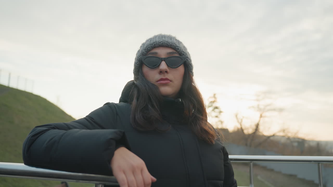 Nighttime rooftop performer. Confident dancer on city rooftop. Reflective performer with stylish accessories under cloudy sky. Elegant dancer in winter coat gazing thoughtfully at moody evening sky