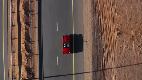 tracking shot of a red cabriolet car driving on desert road in summer - aerial top view