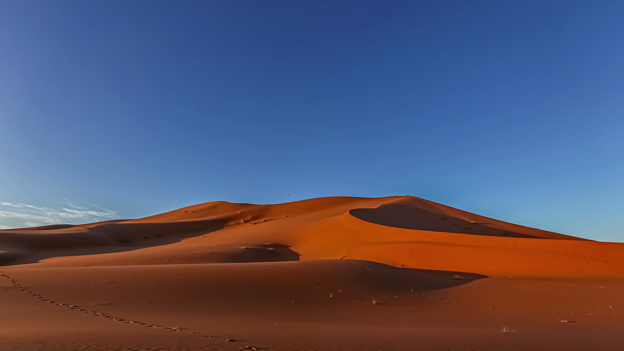 Time lapse shot of beautiful sunrise over Desert of Morocco during sunny day - Sand dunes lighting in orange colors against blue sky