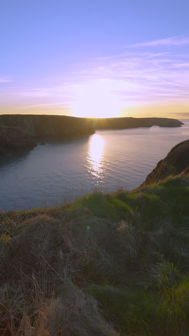 Vertical Video of Sunset Over Pembrokeshire Welsh Coastline from Coast Path with Sun Reflection on Water and Brightly Colored Sky with Setting Sun