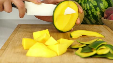 cortar mango en trozos más pequeños en una tabla de cortar de madera, usando un cuchillo de cerámica afilado