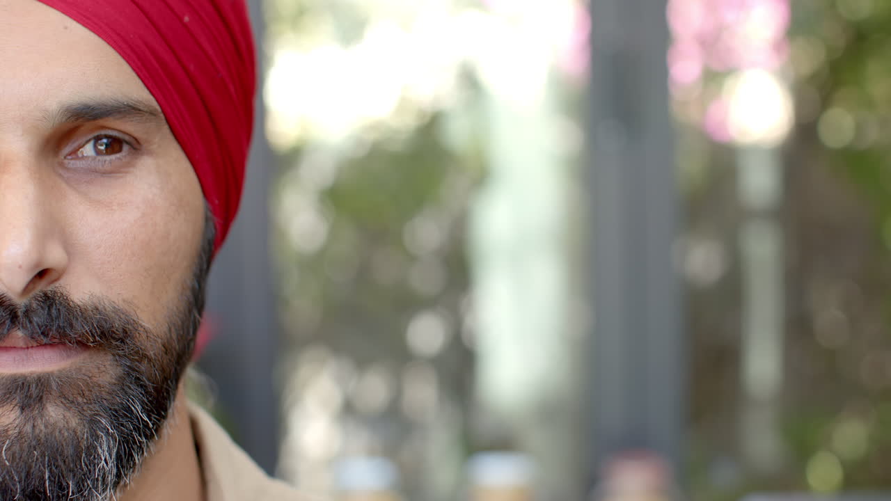 Close-up of man wearing red turban and beard, looking at camera outdoors
