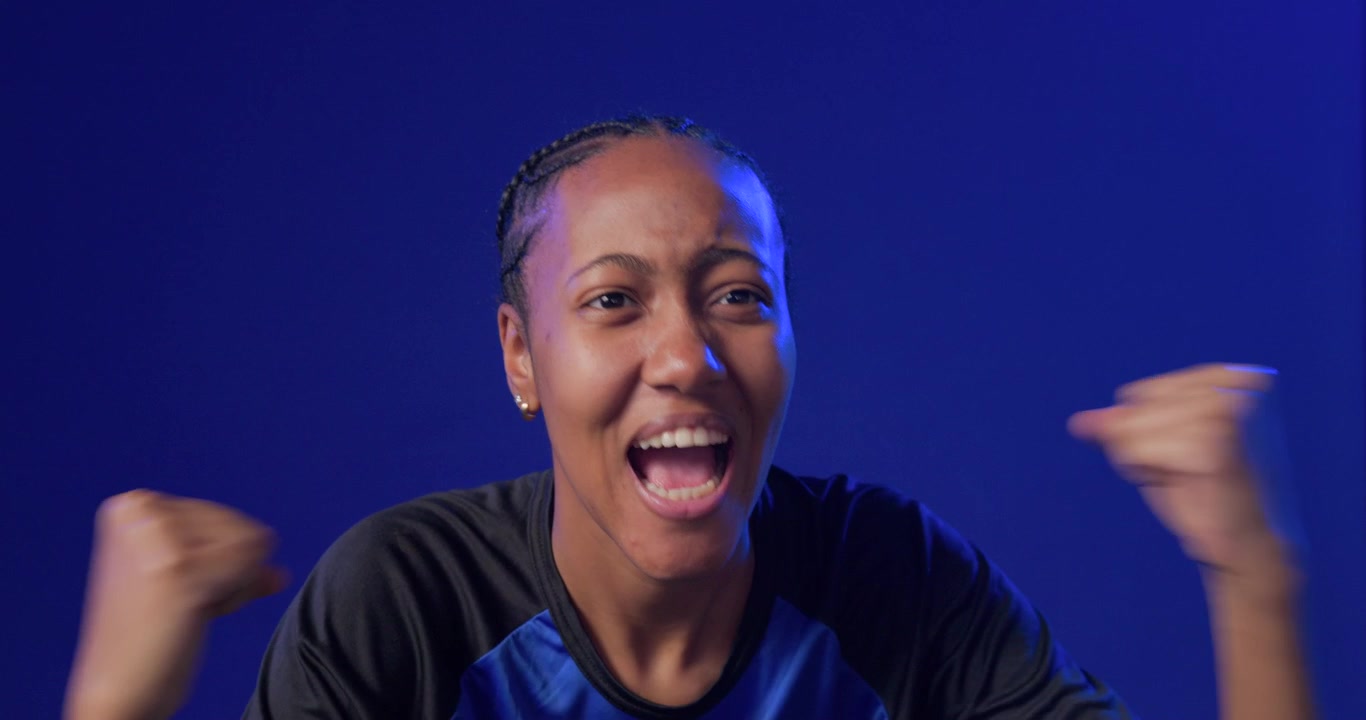 Donna afroamericana che reagisce a un segnale, urlando, gesticolando e sorridendo, su sfondo blu, indossando una camicia.