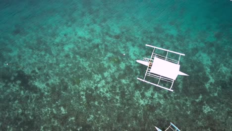 Bangka-boats-floating-on-crystal-clear-water-in-Philippines,-approaching-drone-overhead-shot