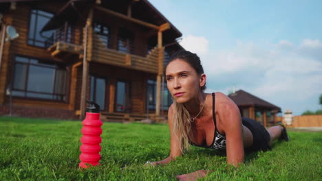 hermosa morena en el fondo de una gran mansión dedicada al fitness y realiza ejercicios de tabla para la prensa, entrenando al aire libre