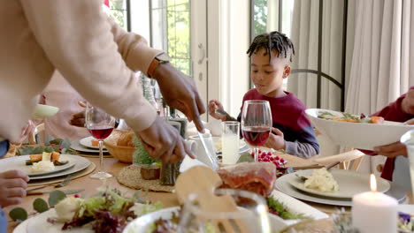 african american father carving meat at multi generation family christmas dinner table