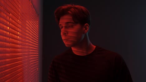 young man looking through window in red light