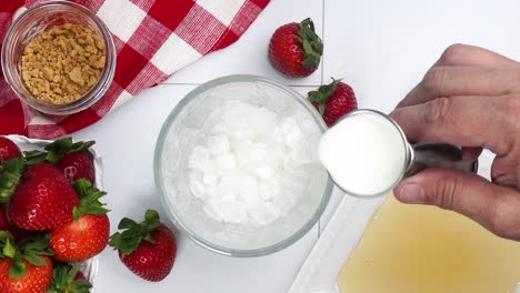 making a strawberry shortcake martini and adding in the heavy cream with the other ingredients. strawberries on a red and white gingham napkin. close up of making a cocktail for happy hour.