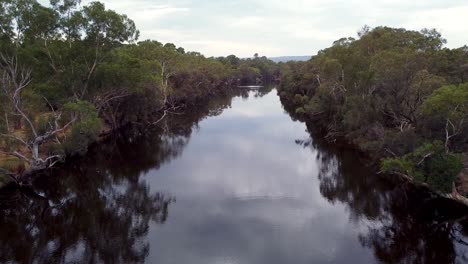 Narrow-river-reflects-the-trees-on-either-side-of-the-water,-aerial