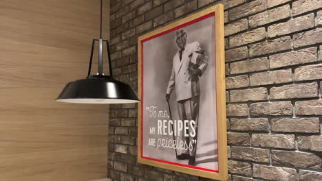 framed photograph of the kfc owner hanging on the wall. colonel sanders pictures on the brick wall. to me, my recipes are priceless. framed black and white photography.