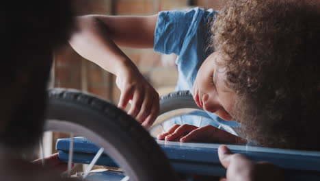 pre teen boy screwing in a bolt with help from his dad while making a racing kart in the garage, close up, selective focus